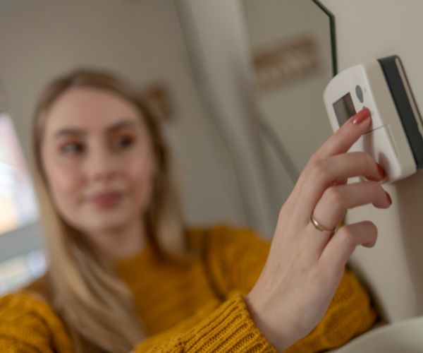 Woman changes the settings on a thermostat, central heating by Thomas Faull