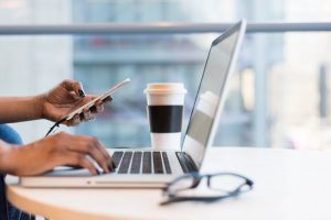 woman using laptop with phone in hand